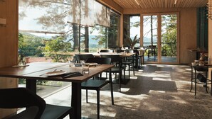 Un restaurant doté de nombreuses tables et chaises, de grandes fenêtres donnant sur l’extérieur et d’un plafond en bois.