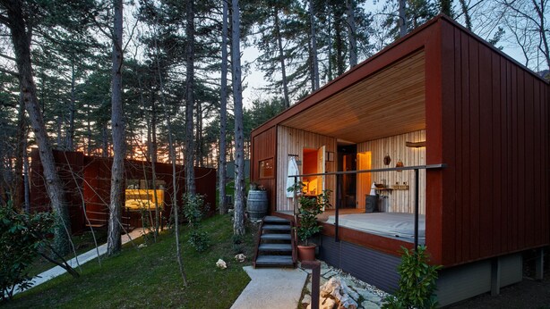 Une cabane moderne avec une façade en bois, une véranda et un chemin de pierre menant à l’entrée.