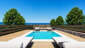 A pool with lounge chairs, a wooden deck, and a view of the sea. - Villa Liana - One Bedroom Villa, Sleeps 2 (Petalidi)