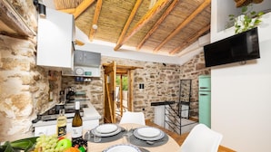 Un coin repas chaleureux avec un mur en pierre, des poutres en bois au plafond et, au fond, une cuisine moderne.
