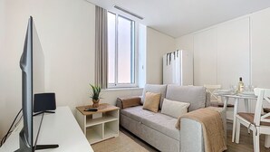 Una sala de estar moderna con un sofá gris, una mesita con una planta, un televisor y un comedor con sillas y una mesa.