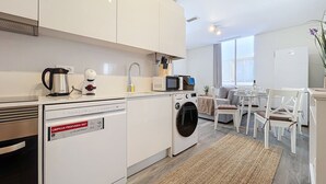 Una cocina moderna con armarios blancos, lavadora, cafetera y microondas.