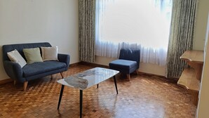 Ein Wohnzimmer mit einem dunkelblauen Sofa, einem Glastisch und einer Holzbank.