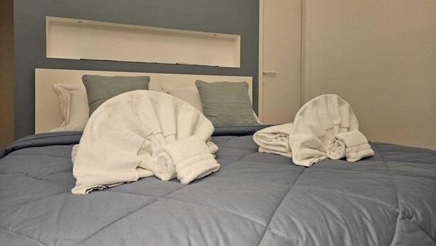 A neatly made bed with a grey duvet and two folded towels on it.