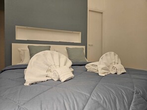 A neatly made bed with a grey duvet and two folded towels on it.