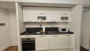 A compact kitchen with white cabinetry, a black countertop, a stove, a microwave, and a sink.