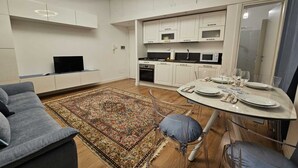 A modern kitchen with white cabinets, a dining table set for four, and a TV on a stand.