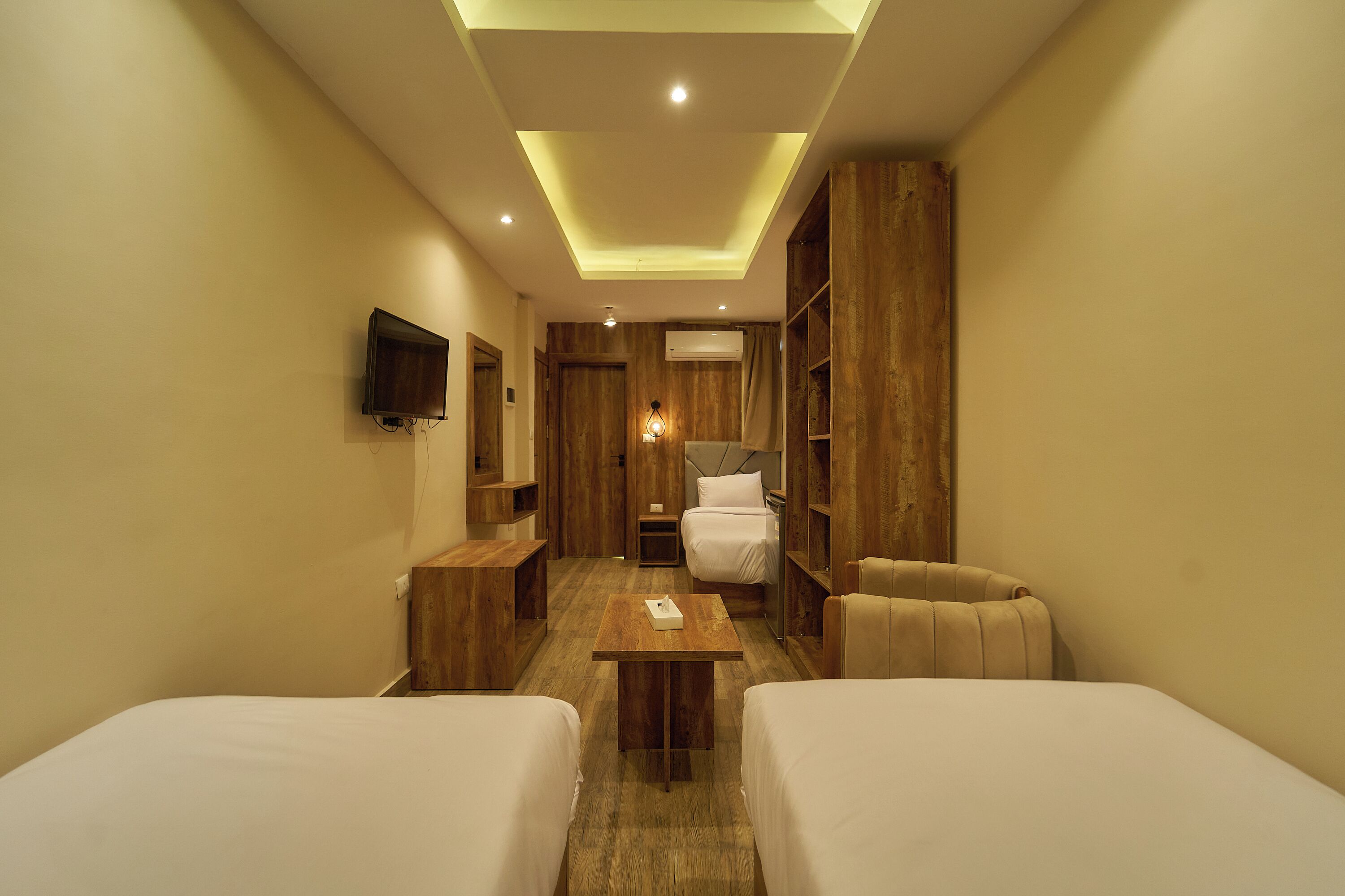 Una habitación de hotel con dos camas, una mesa de madera, un televisor montado en la pared y un armario.