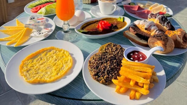 A breakfast table with various dishes and a glass of orange juice, set on a balcony with a view of pyramids. - Crown Pyramids View Hotel (Giza)