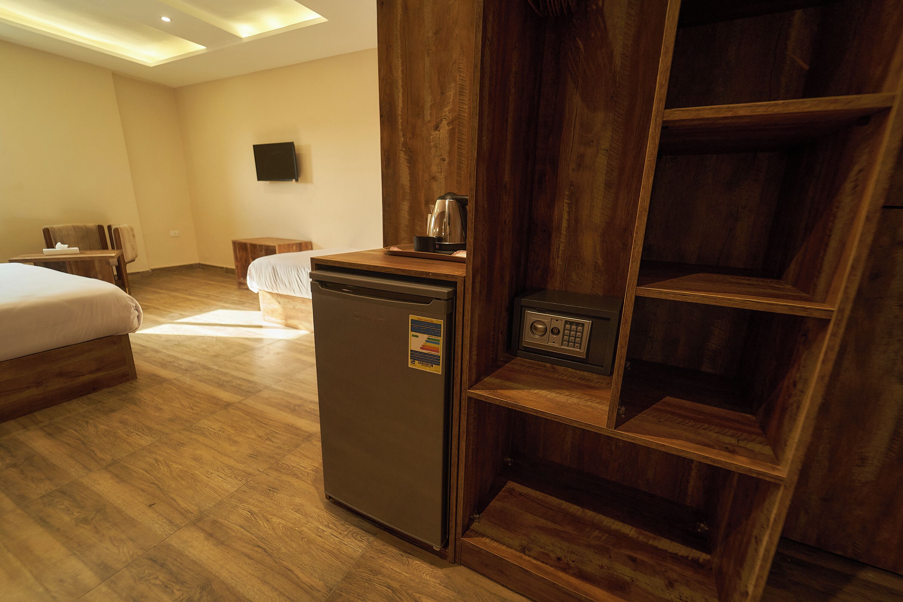 A hotel room with a bed, a small desk, a refrigerator, a coffee maker, and a wooden shelf unit.