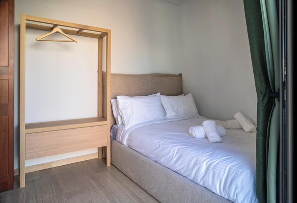 A bedroom with a bed, a wooden wardrobe, and a hanging clothes rack.