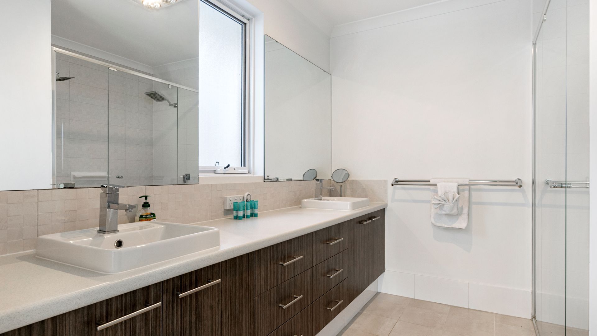 A modern bathroom with two sinks, a large mirror, and a glass shower enclosure.