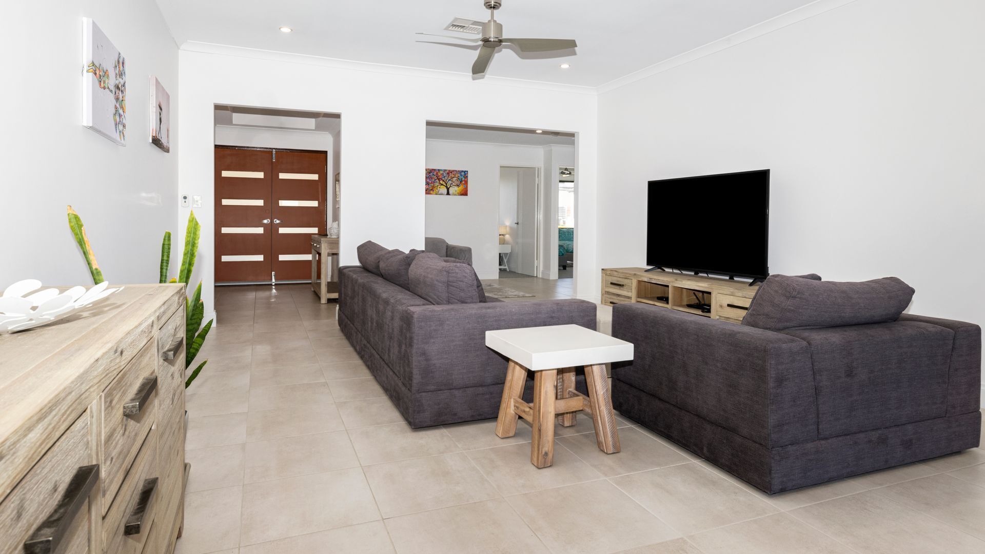 Un salon moderne avec deux canapés gris, une table basse blanche, un meuble TV en bois et un ventilateur de plafond.