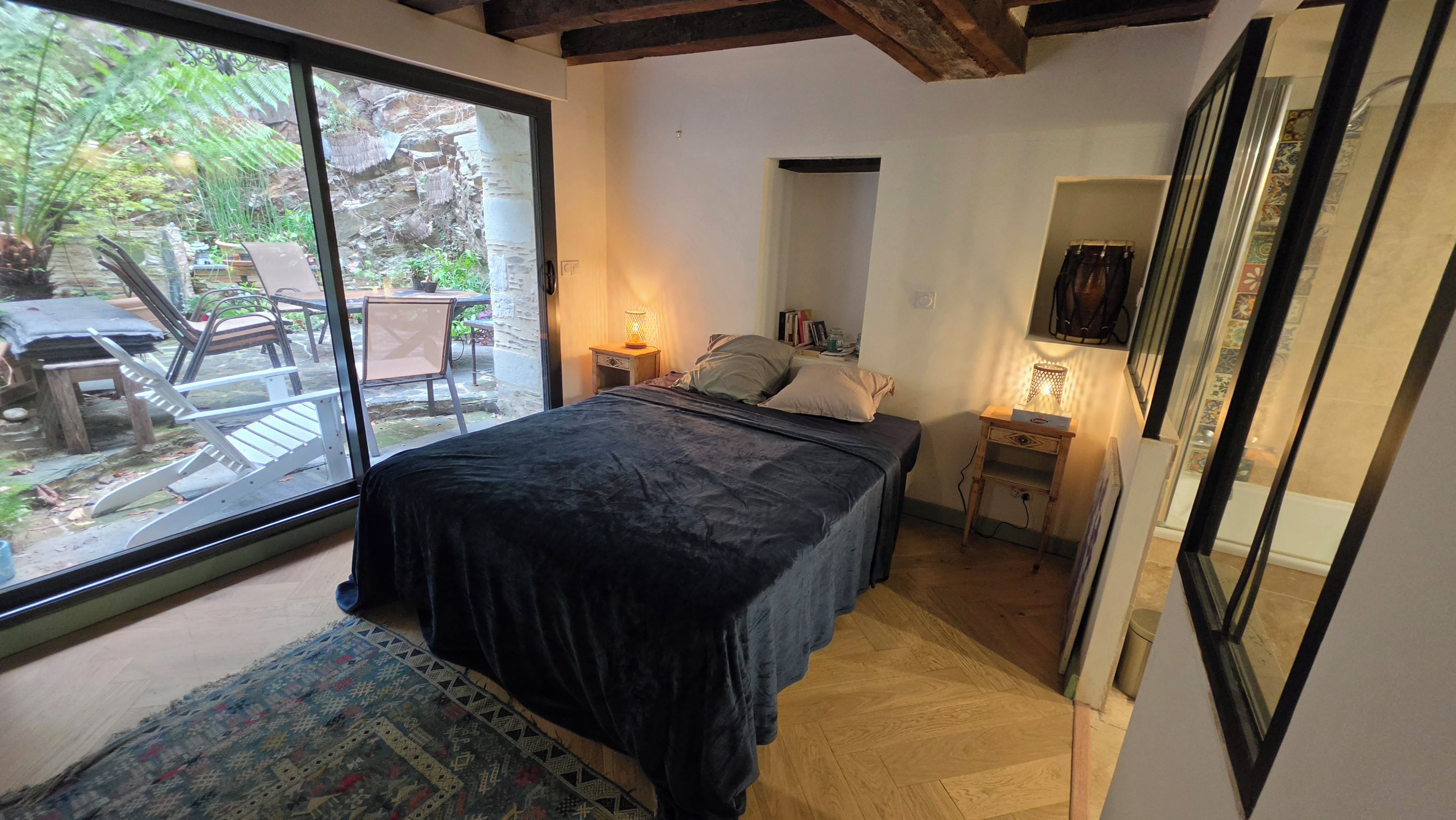 Un dormitorio con una cama grande, una mesita de noche con lámpara, un estante pequeño y vistas a un patio exterior con sillas y una mesa.