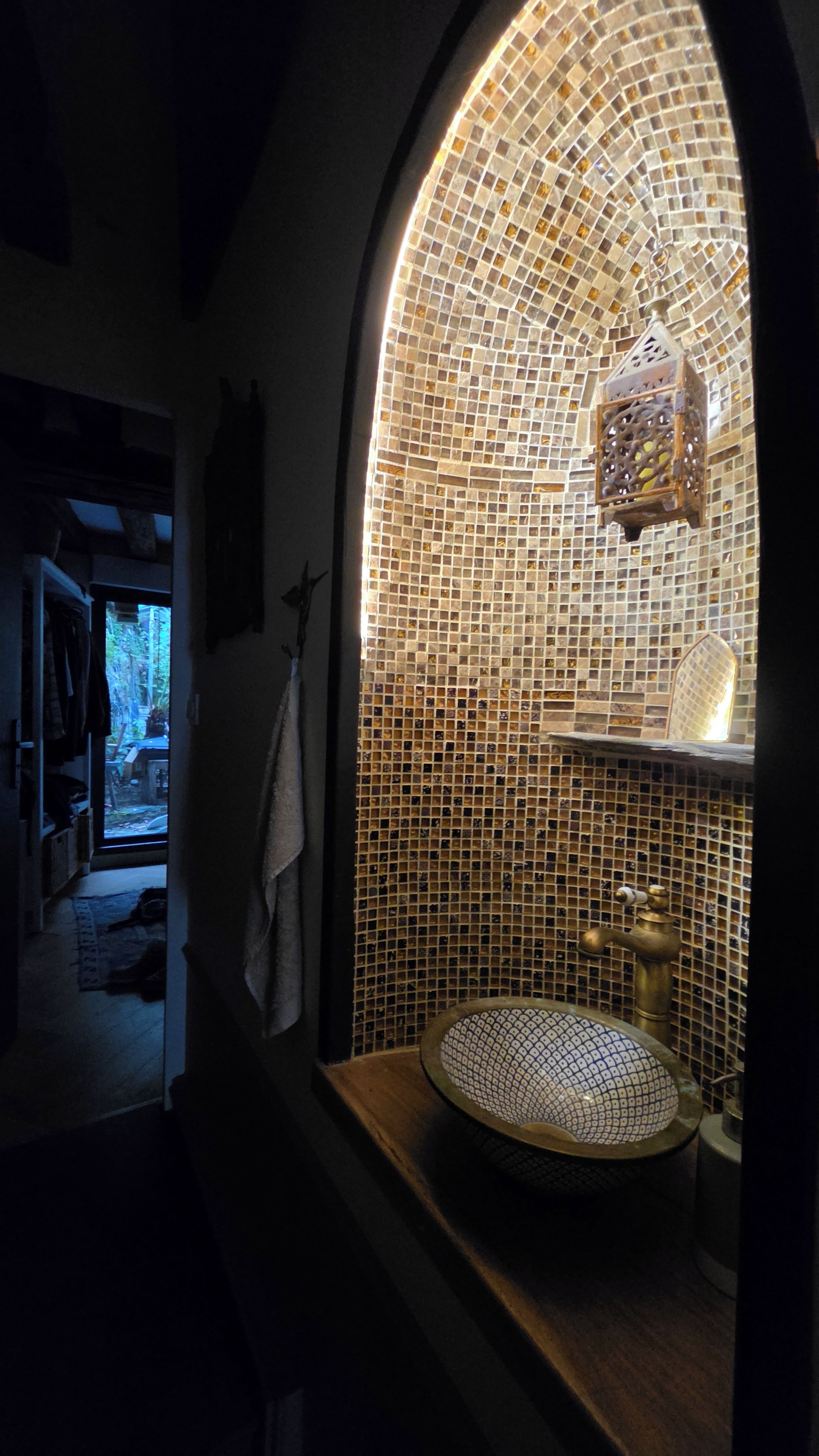 Un bany amb una paret de mosaic, un lavabo amb una bassina decorativa i un llum de lanterna penjant.