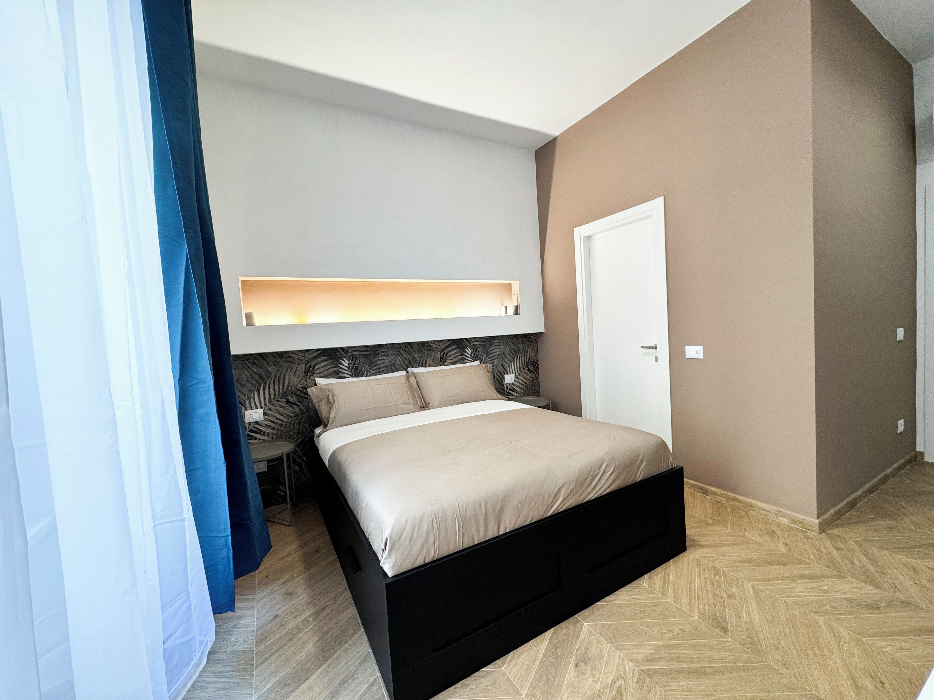A bedroom with a bed, a nightstand, a wall-mounted light, and a door.