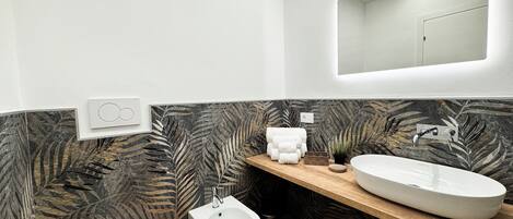 A modern bathroom with a marble-patterned wall, a wooden vanity, a white sink, a bidet, and a toilet.