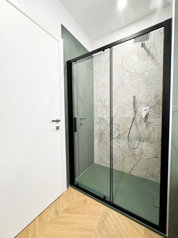 A modern shower enclosure with a glass door and a leaf pattern on the wall.