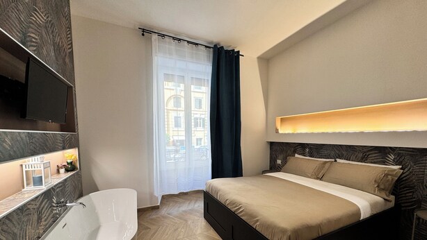 A modern bedroom with a large bed, a bathtub, and a window with curtains. - ALL IN ROME RE DI ROMA (Rome)