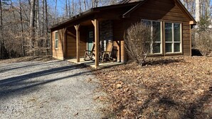 A rustic cabin with a porch, a small deck, and a stone foundation.