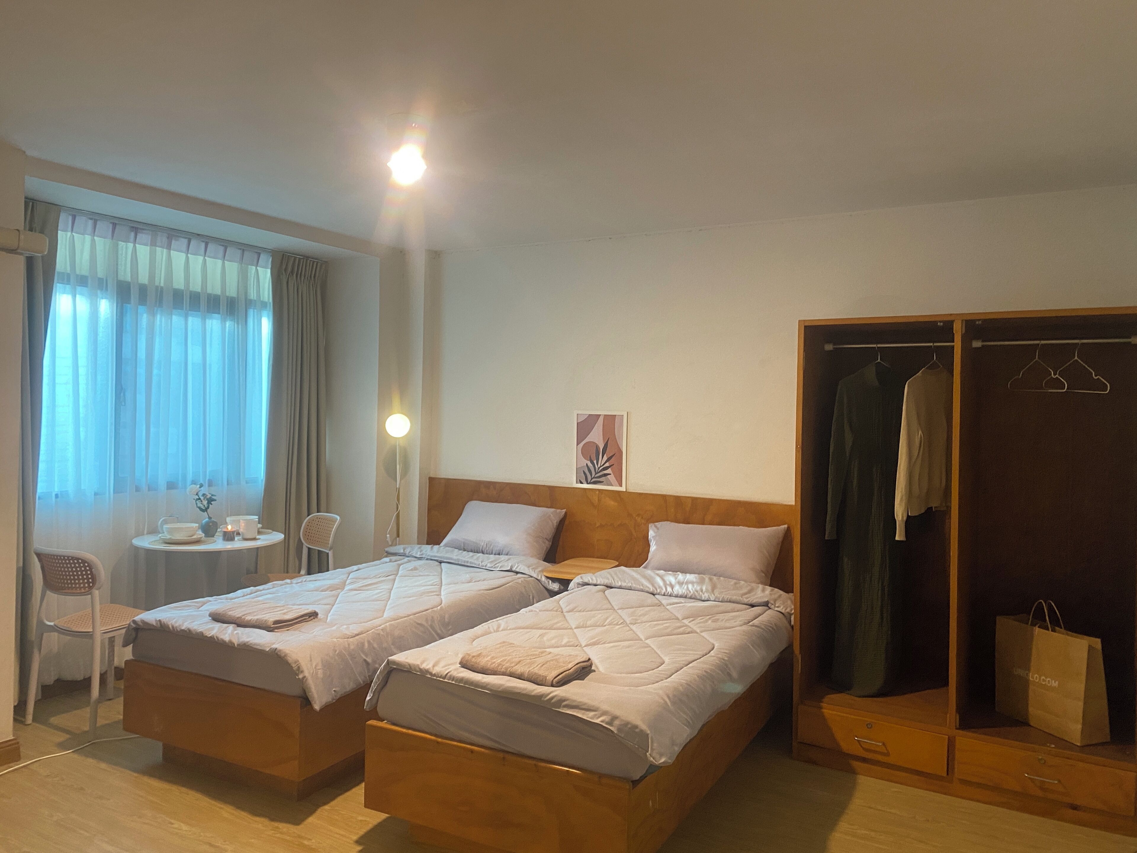 Habitación de hotel con dos camas, una mesita con una silla, un armario y una ventana con cortinas.