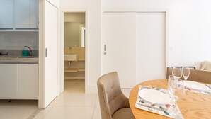 A modern dining area with a round wooden table set for two, a beige upholstered chair, and a white door in the background.