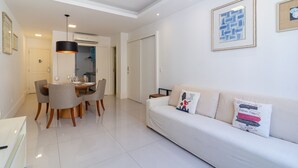 A modern living room with a white sofa, a dining table with chairs, and a kitchen area in the background.