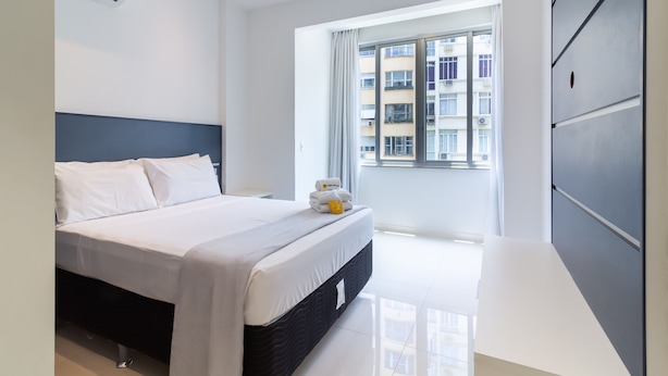A modern hotel room with a large bed, a window with curtains, and a view of a building outside.