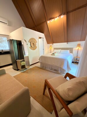 A hotel room with a bed, bedside lamps, a wall clock, a small table, and a seating area. - Cabana Mulungu (Fernando de Noronha)