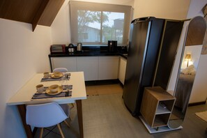 Une cuisine compacte comprenant un réfrigérateur, une petite table à manger avec des chaises et une fenêtre donnant sur les arbres.