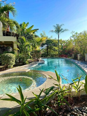 A swimming pool surrounded by tropical plants and a building with a balcony. - Coco Sunset Hills #42 (Playas del Coco)