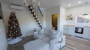 A modern living room with a white sectional sofa, a staircase with black railings, and a Christmas tree. - Woodland Nook (Alpine)