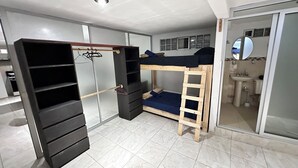 Une chambre avec un lit superposé, une armoire avec plusieurs étagères, un miroir et une salle de bain équipée d’un lavabo et de toilettes.