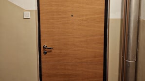 Une porte en bois avec un cadre noir, une petite étiquette au-dessus, et un interrupteur sur le mur, à gauche.
