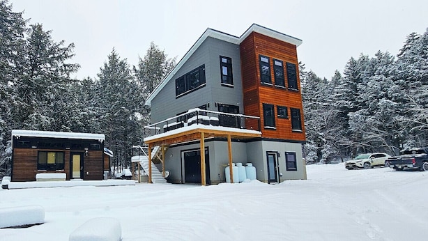 Ein modernes, zweistöckiges Haus mit überdachter Veranda und Garage, umgeben von schneebedeckten Bäumen.