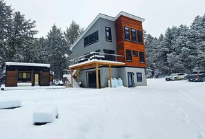 Ein modernes, zweistöckiges Haus mit überdachter Veranda und Garage, umgeben von schneebedeckten Bäumen.