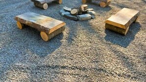 Ein Kiesbereich mit vier Holzbanken und einem Holzstoß in der Mitte.