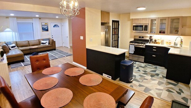 Een moderne keuken met een centraal eiland, roestvrijstalen apparatuur en een eethoek met een houten tafel en stoelen.
