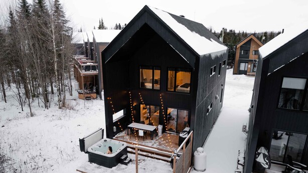 Una cabaña moderna con una terraza amplia, mobiliario exterior y un jacuzzi.