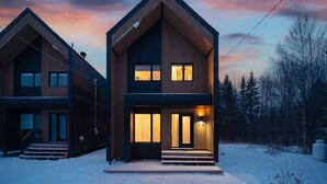 Una casa moderna de dos pisos con un diseño simétrico, que presenta una entrada central con escalones y una puerta principal iluminada.