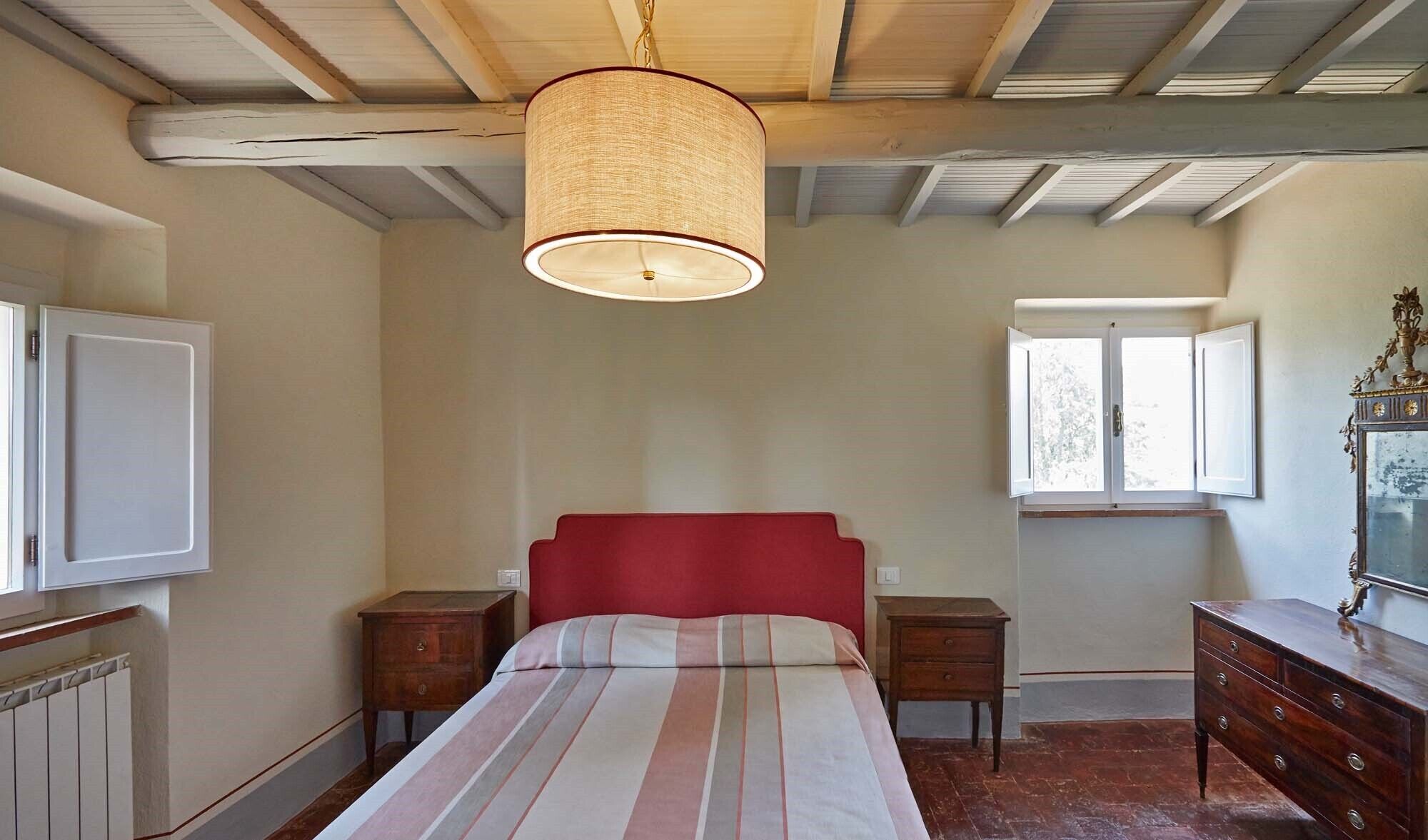 A bedroom with a bed, two nightstands, a dresser, a window, and a ceiling fan.