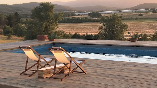 Una terraza de madera con dos sillones reclinables y una piscina.