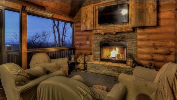 A cozy log cabin interior with a fireplace, two sofas, and a large window overlooking a forested area. - Beautiful, private, Blue Ridge, GA cabin with incredible views.  (Blue Ridge)