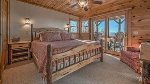 A bedroom with a wooden bed, a nightstand, a lamp, and a view through large glass doors. - Beautiful, private, Blue Ridge, GA cabin with incredible views.  (Blue Ridge)