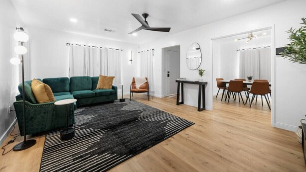 Un salon moderne avec un canapé vert, un coin repas comprenant une table et des chaises, et un ventilateur de plafond.