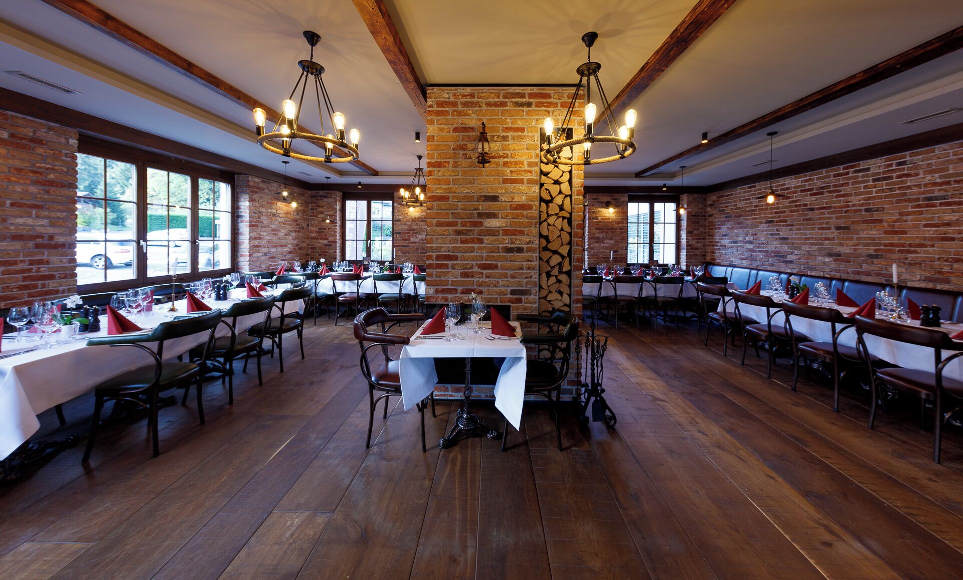 A restaurant with brick walls, wooden floors, and multiple tables set for dining.