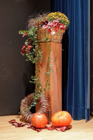 A decorative arrangement with a basket of flowers, a wreath, and pumpkins on a wooden surface. - BERG & BERG Hotel - Hellbühl Self-Check-in (Neuenkirch)