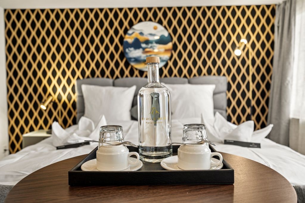 A neatly arranged breakfast tray on a bed with a decorative headboard and a painting in the background.