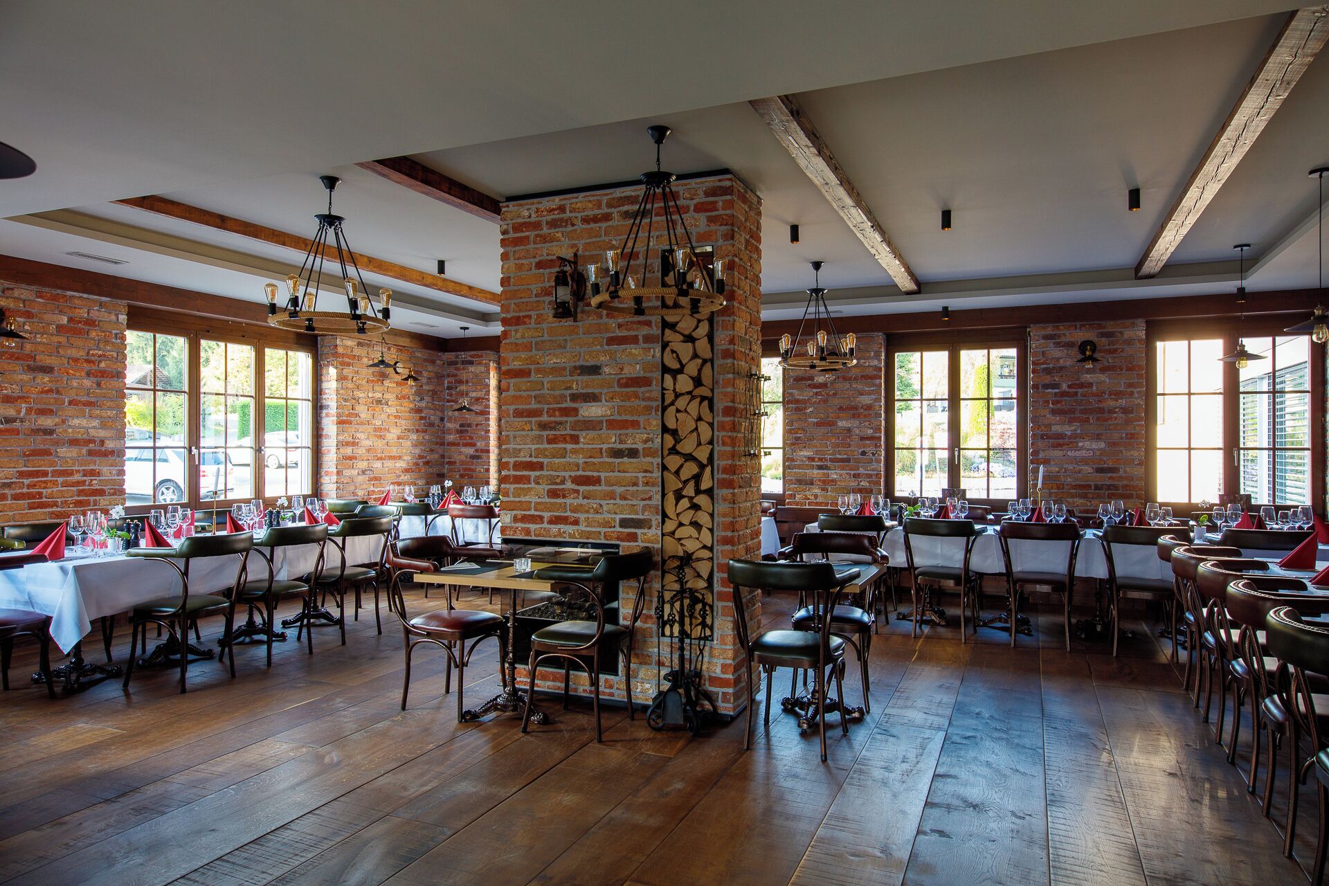 Un restaurante con paredes de ladrillo, suelos de madera y varias mesas de comedor con sillas y servilletas rojas.