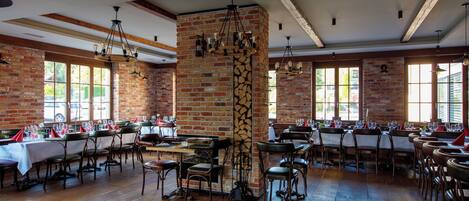 Un restaurante con paredes de ladrillo, suelos de madera y varias mesas de comedor con sillas y servilletas rojas.